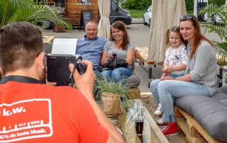 Ein Fotograf von Radio K.W. fotografiert eine sitzende Gruppe von Hörerinnen und Hörern für die Polaroid-Aktion.